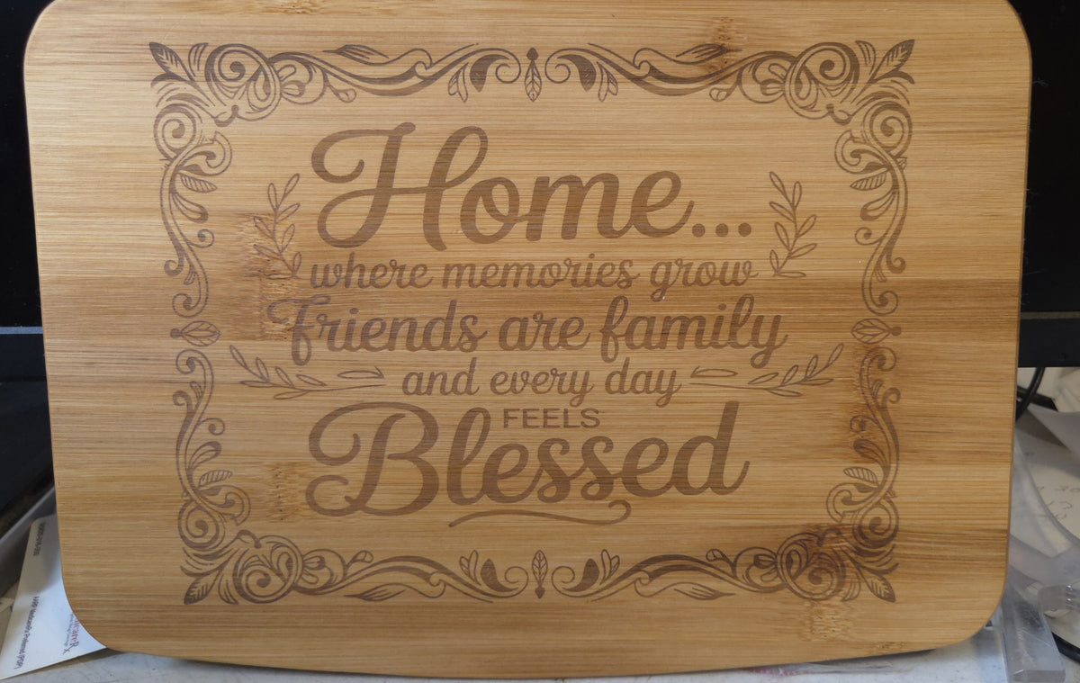 A rectangular bamboo cutting board with rounded corners, featuring a laser-engraved decorative border and the quote 'Home where memories grow