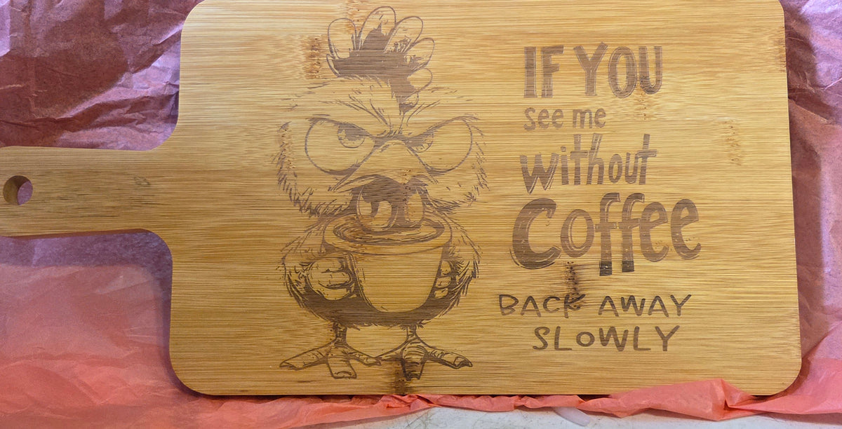 A rectangular wooden cutting board with a handle, featuring a cartoon chicken holding a coffee cup and the engraved text 'IF YOU see me without Coffee BACK AWAY SLOWLY'. The board is photographed on pink tissue paper.